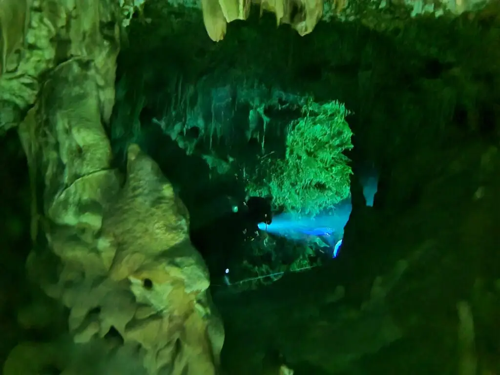 Diver light in a green cavern passage of a Riviera Maya cenote