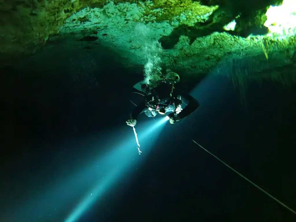 Diver beneath a beam of sunlight in a crystal clear cenote