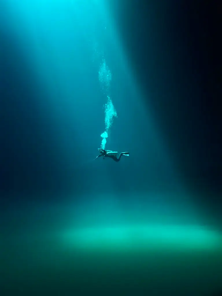 Cenote Diving in the Riviera Maya: The Complete Guide 13 Diver beneath a light shaft in a deep green cenote