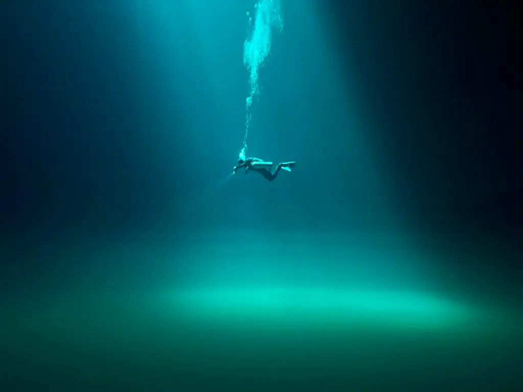 Diver silhouette beneath a light beam in a green-blue cenote