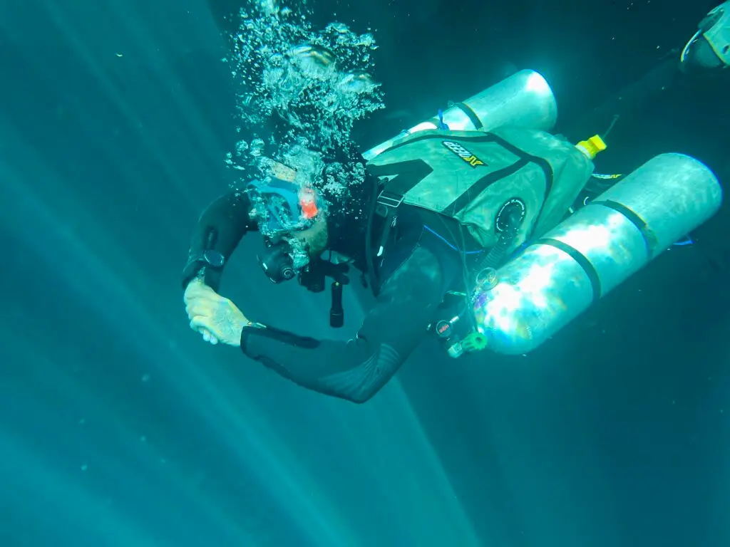 Technical diver with stage tanks in cenote light beams