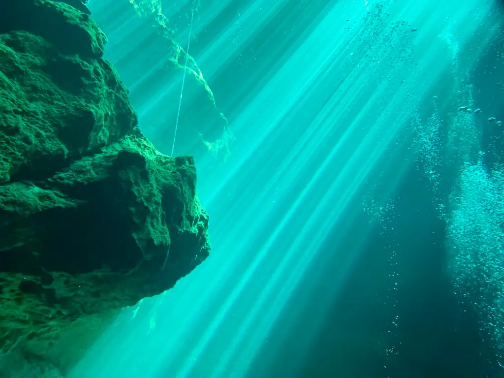 Sunbeams cutting through the clear water of a cenote entrance